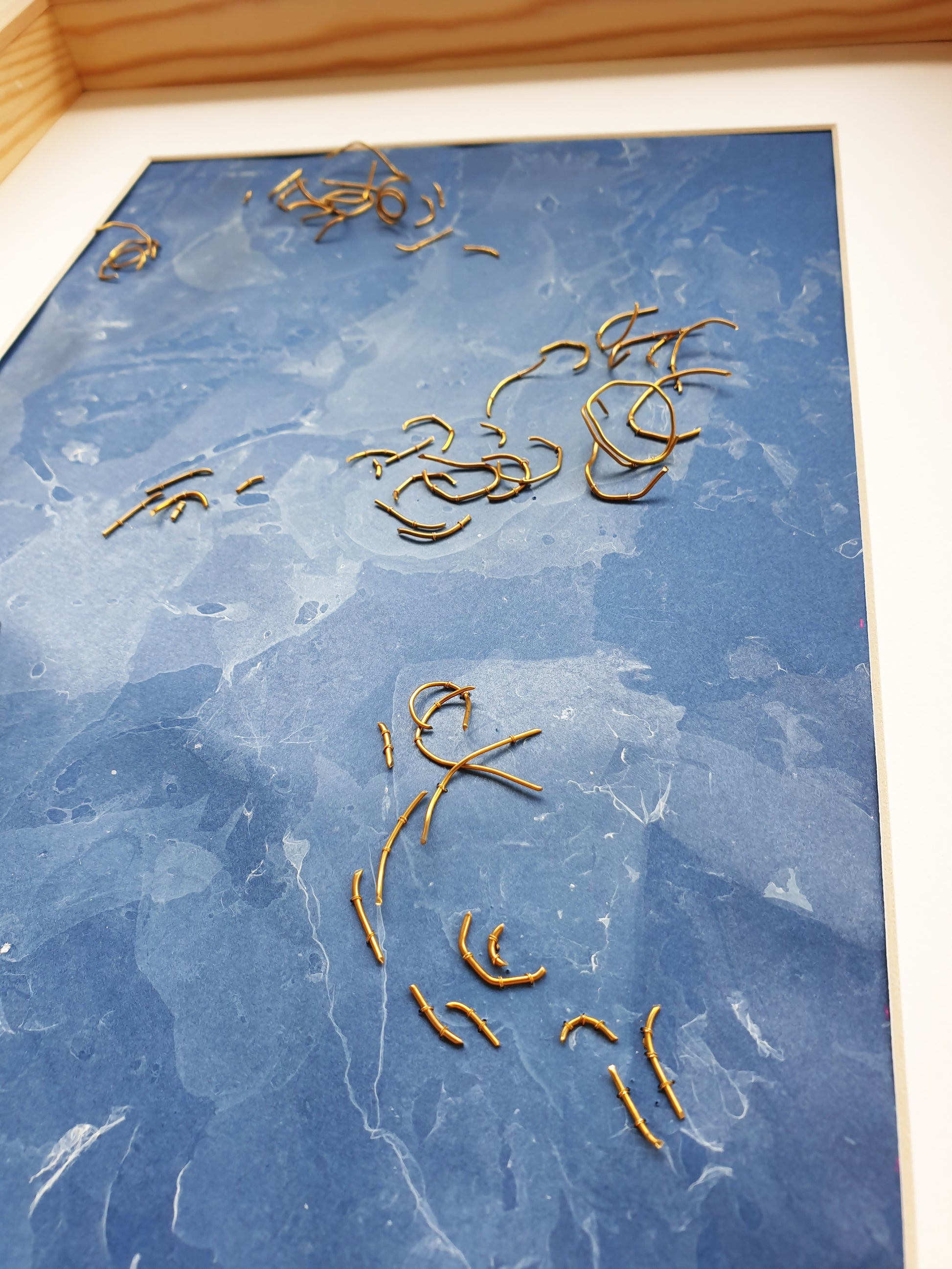 Zoom sur l'oeuvre nommée Eaux Libres. Papier marbré de ton bleue, brodée main avec des fragments de laiton.