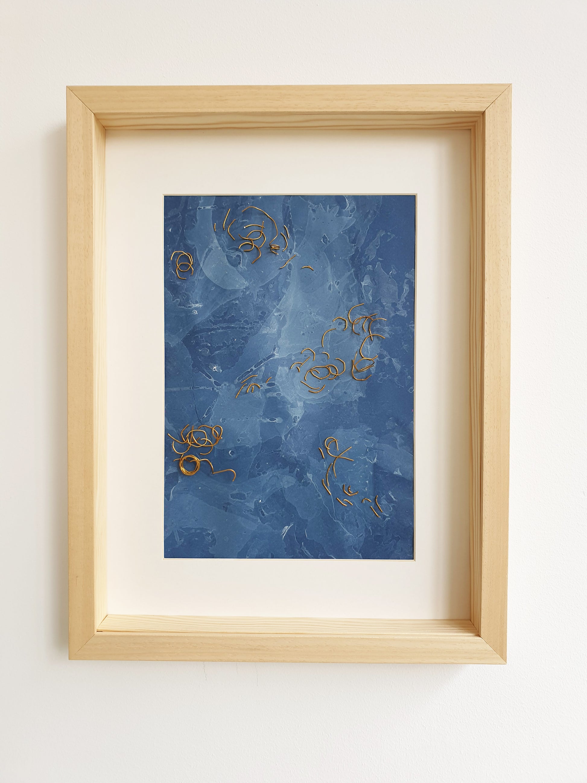 Visuel de l'oeuvre nommée Eaux Libres encadrée. Papier marbré de ton bleue, brodée main avec des fragments de laiton.