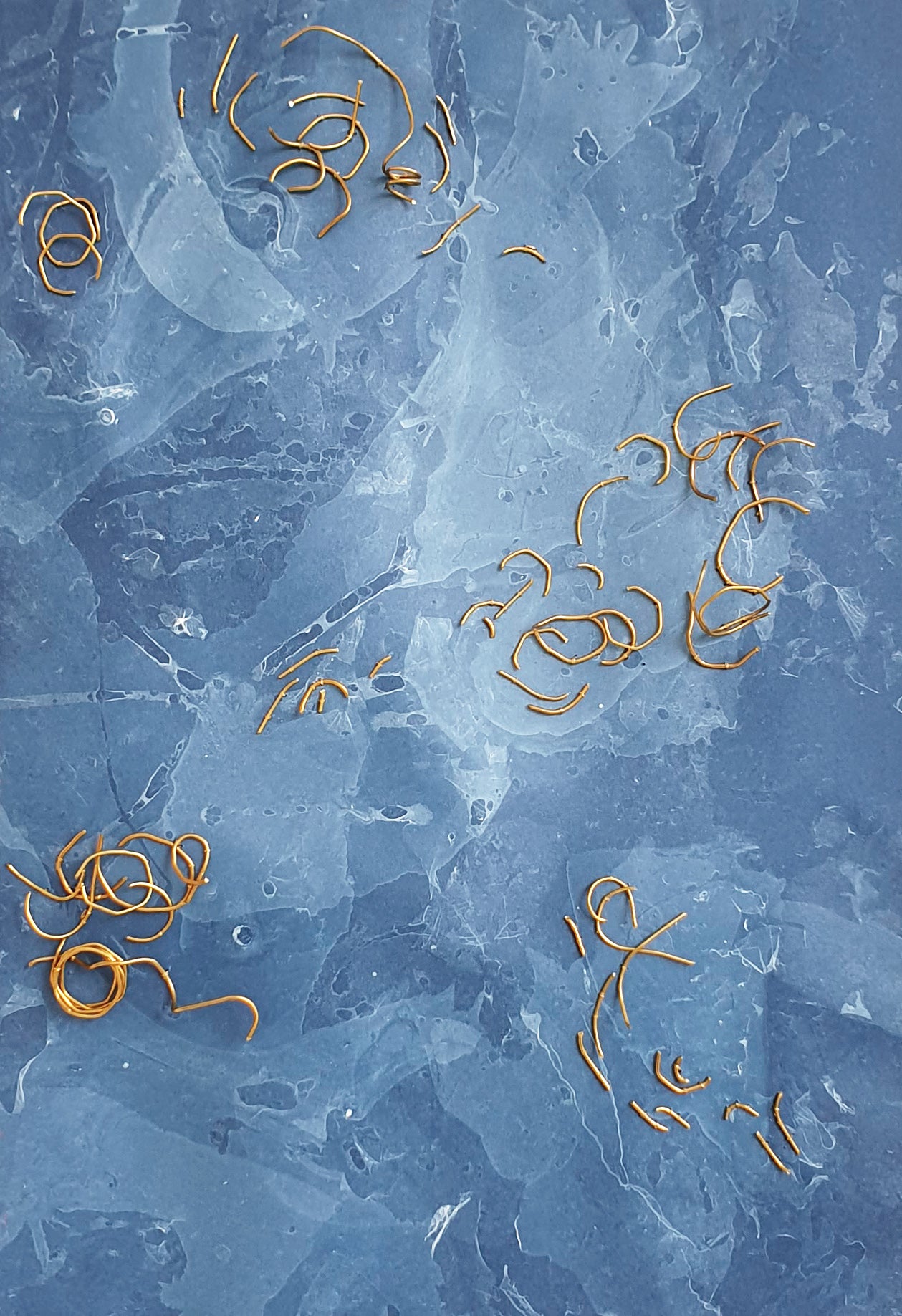 Zoom sur l'oeuvre nommée Eaux Libres. Papier marbré de ton bleue, brodée main avec des fragments de laiton.